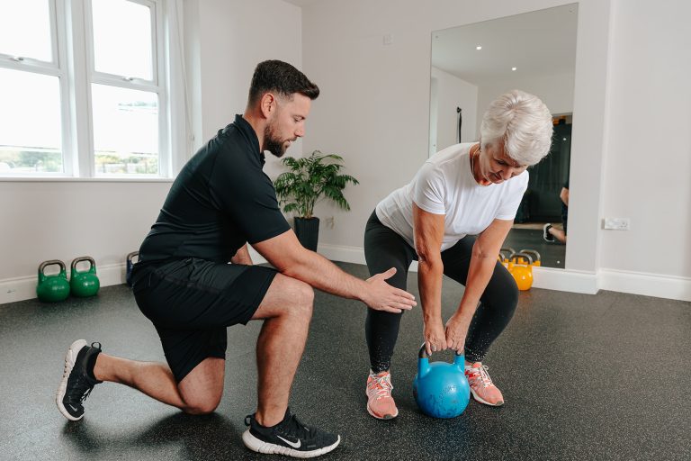 Woman lifting kettlebell weight with trainer